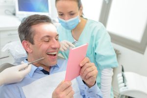 dental assistant showing patient his smile in hand mirror